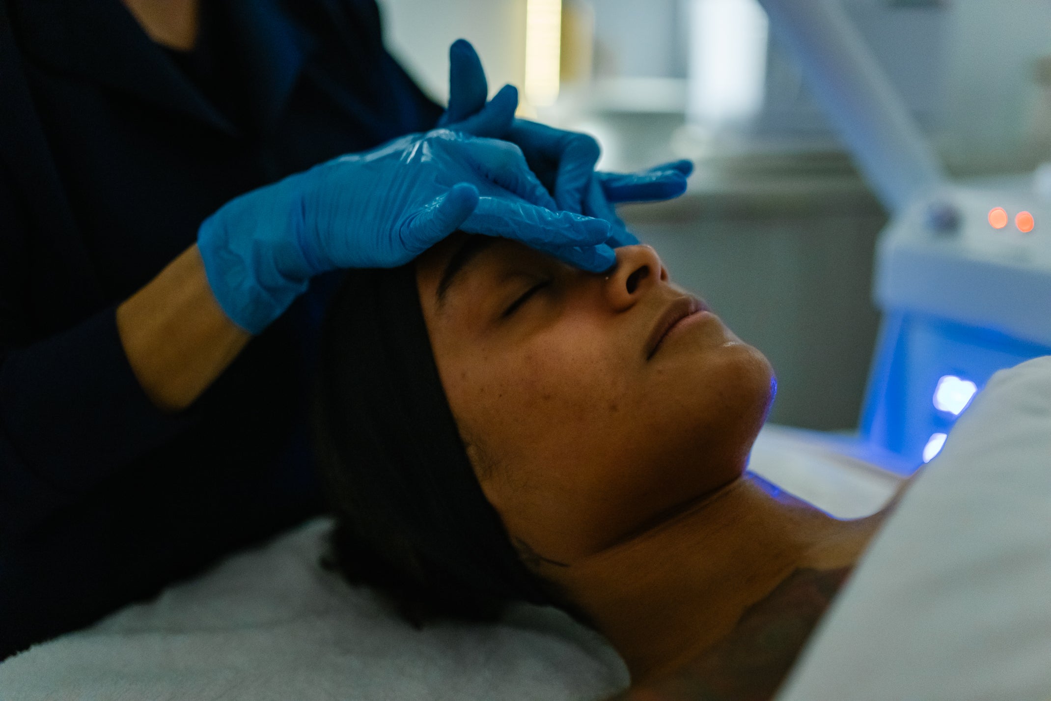 Person receiving a facial treatment with blue gloves and a machine in the background