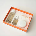 A skincare gift set by THESS from their Lotus Collection, presented in an orange box with a white insert. The set includes a large clear bottle of toner, a smaller clear bottle of essence, a white round jar, and a small clear pouch containing a gold-toned hair tool, all on a light gray background.